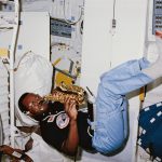 Astronaut floating in the space shuttle cabin playing a small saxophone